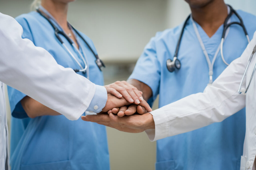 Mature,Doctors,And,Young,Nurses,Stacking,Hands,Together